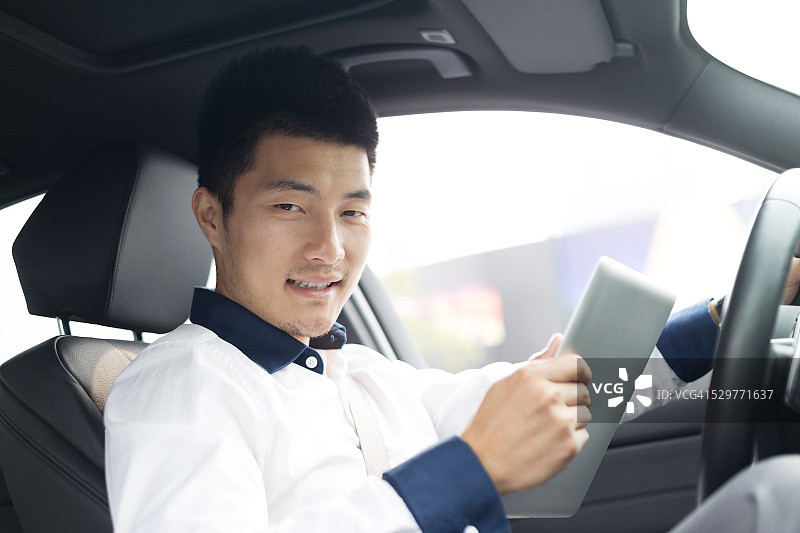 在车里使用智能平板电脑的亚洲年轻男商人图片素材