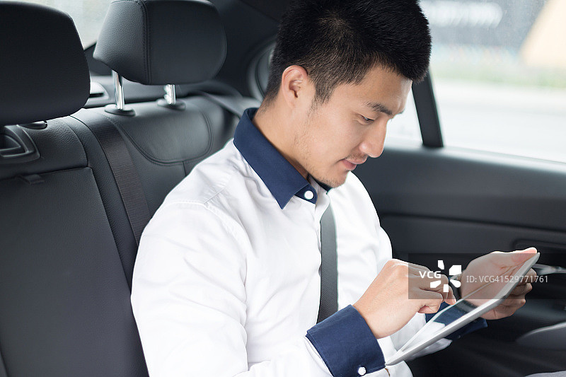 在车里使用智能平板电脑的亚洲年轻男商人图片素材