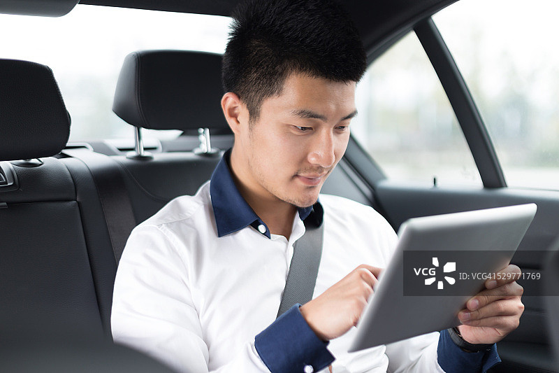 在车里使用智能平板电脑的亚洲年轻男商人图片素材