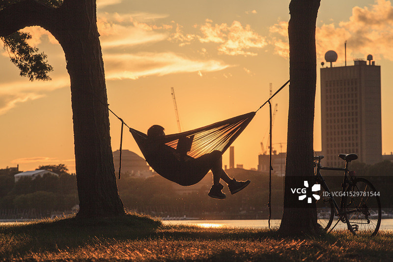 男人在查尔斯河滨广场吊床上看书图片素材