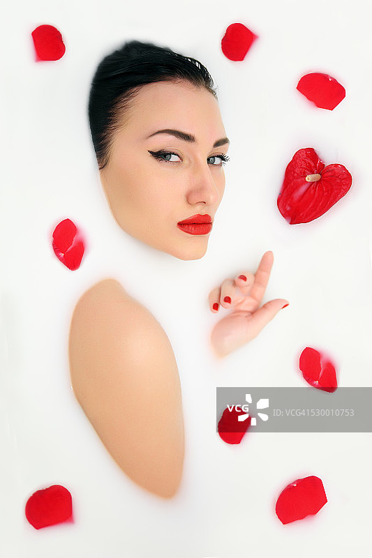 在牛奶浴中红花瓣的时尚女人图片素材