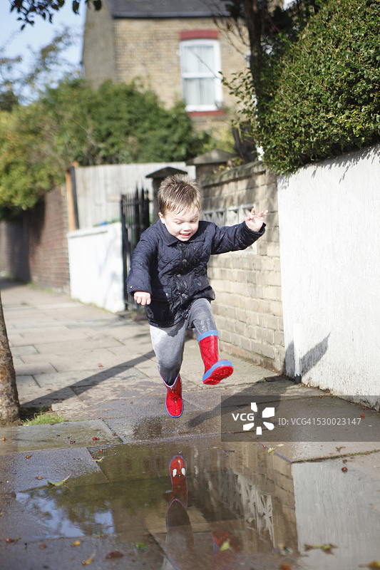 穿红色雨靴的男童在人行道水坑里跳跃图片素材