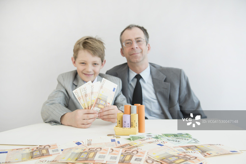 父亲和儿子拿着欧元、纸币和硬币卷的肖像图片素材