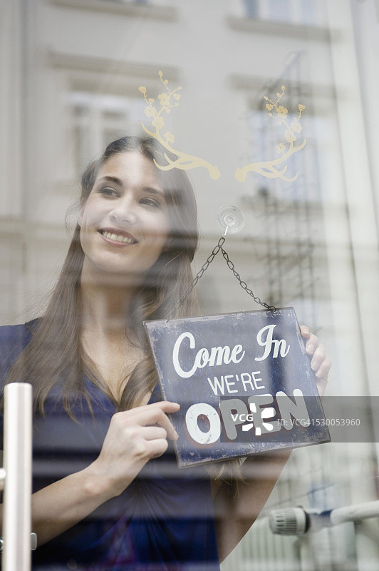 销售员拿着时尚店的开业板，面带微笑图片素材