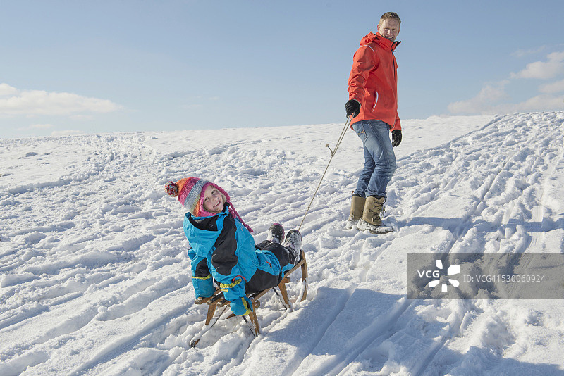父亲在德国巴伐利亚用雪橇拉着女儿，面带微笑图片素材
