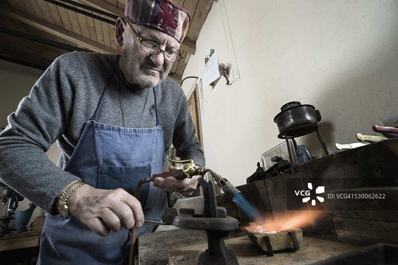 在德国巴伐利亚的工场里用喷灯熔化和浇铸的年长的男金匠图片素材