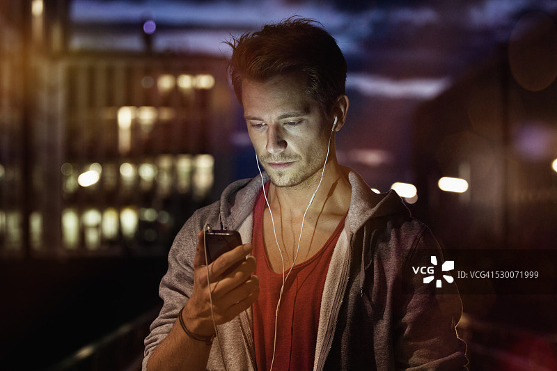 夜晚用智能手机和耳机听音乐的年轻男子肖像图片素材