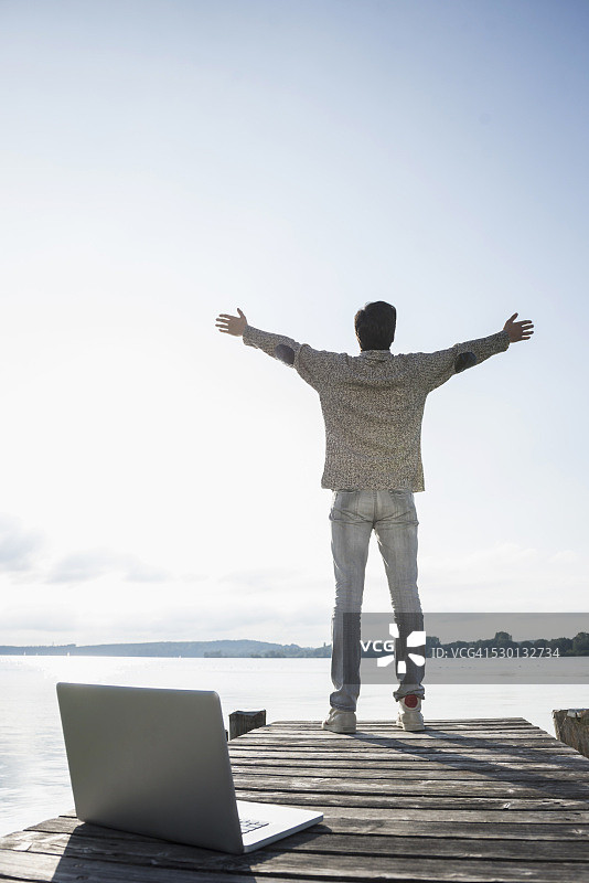 男人在木制码头上用笔记本电脑工作，很愉快图片素材