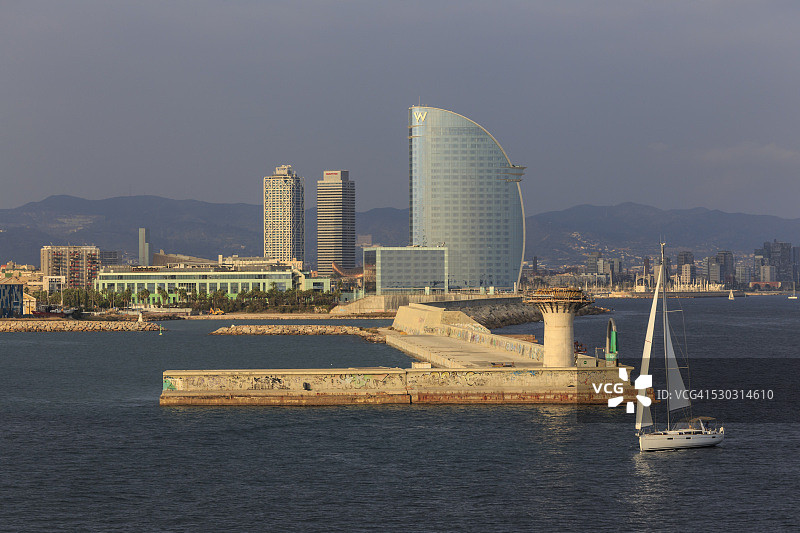 游艇驶过巴塞罗那的La Barceloneta和海滨，远处是奥林匹克港，西班牙加泰罗尼亚图片素材