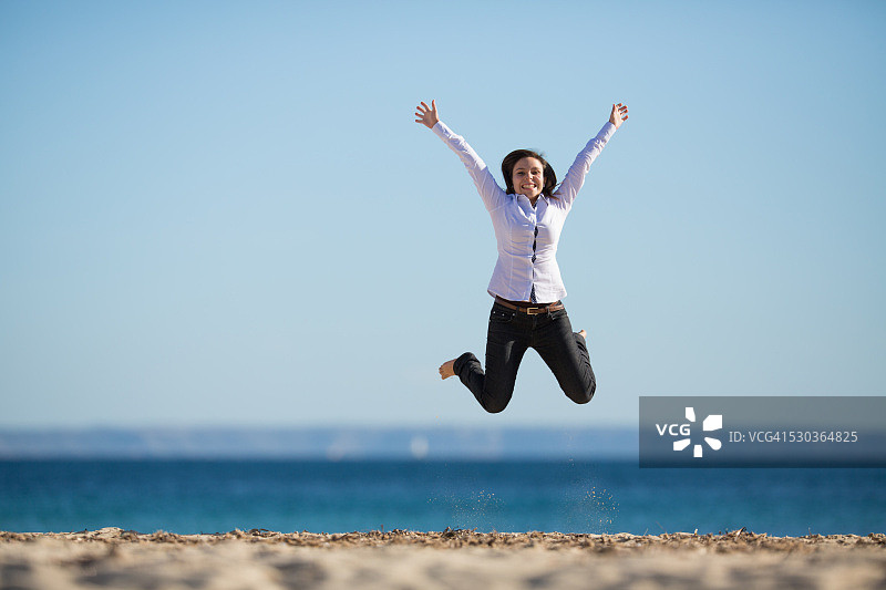 在海滩上跳跃并举起双臂的年轻女子图片素材