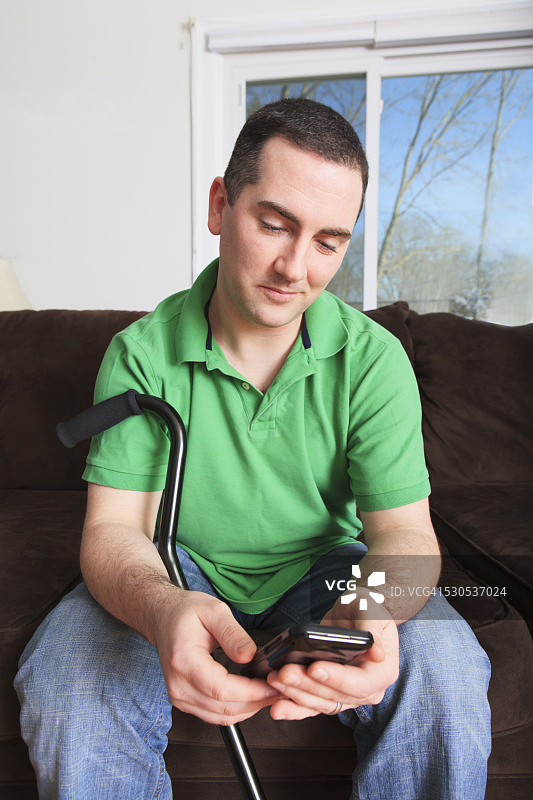 男人在接受前交叉韧带（ACL）手术后拄着拐杖使用智能手机图片素材