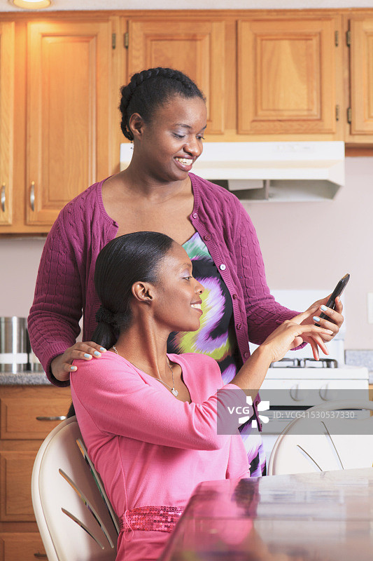 厨房里，两姐妹看着智能手机，其中一个有学习障碍图片素材