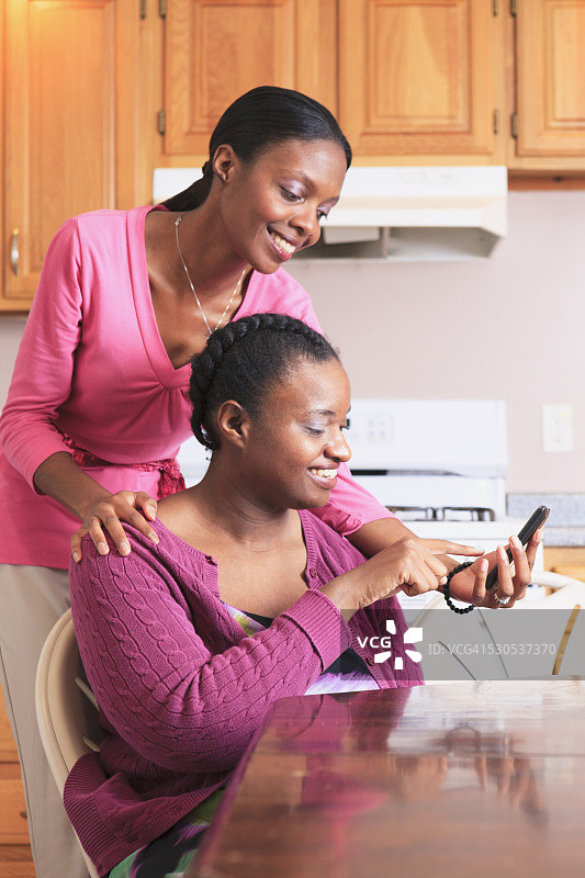 厨房里，两姐妹看着智能手机，其中一个有学习障碍图片素材