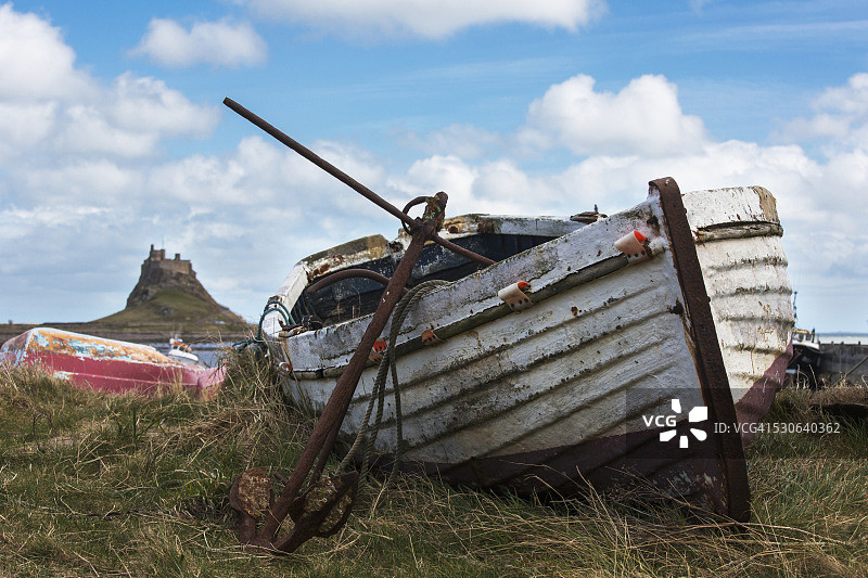 岸边废弃的旧船和生锈的锚，背景是林迪斯法恩城堡，英格兰诺森伯兰郡圣岛图片素材