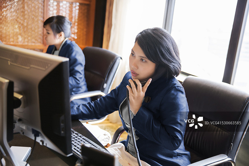 在办公桌前工作的亚洲女性酒店礼宾员图片素材