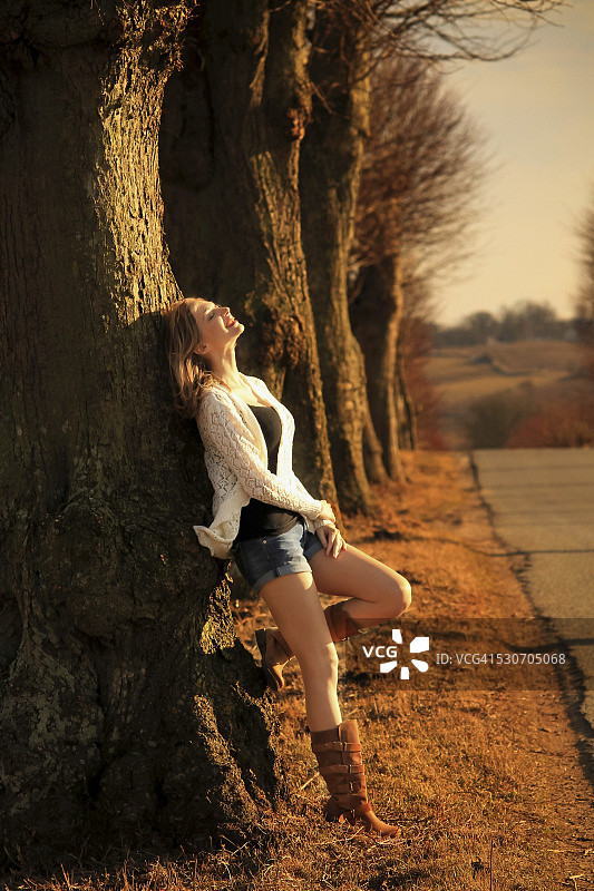 丹麦，欧洲：穿热裤靠在树旁的年轻女人图片素材