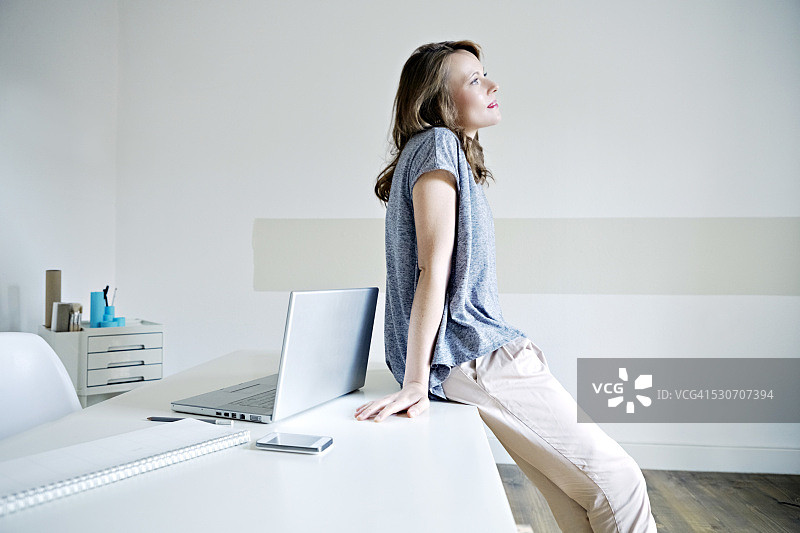 年轻女子在德国巴伐利亚慕尼黑的家中倚靠在桌子上图片素材