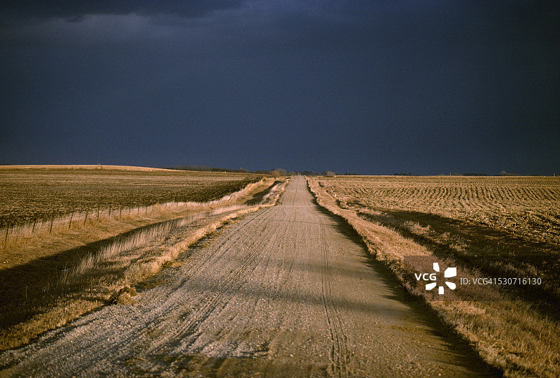 农业：穿过秋季收割后的农田，通往爱荷华州的砾石乡村道路，上方是黑暗的暴风云图片素材
