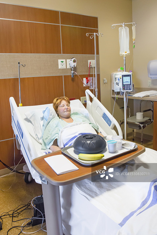 女人躺在医院的病床上，食物托盘未动图片素材