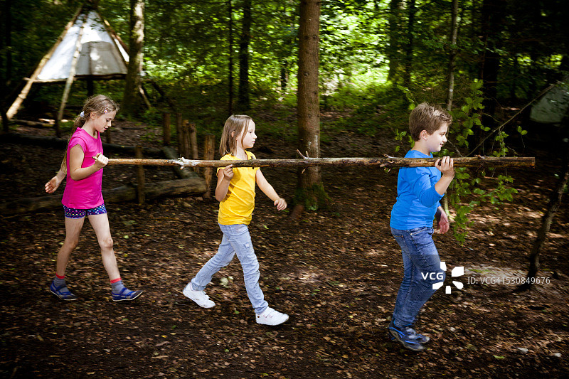 儿童在德国巴伐利亚慕尼黑的森林营地里搬运木头图片素材