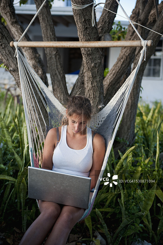 在吊床上使用笔记本电脑的女孩；特克斯和凯科斯群岛南凯科斯岛图片素材
