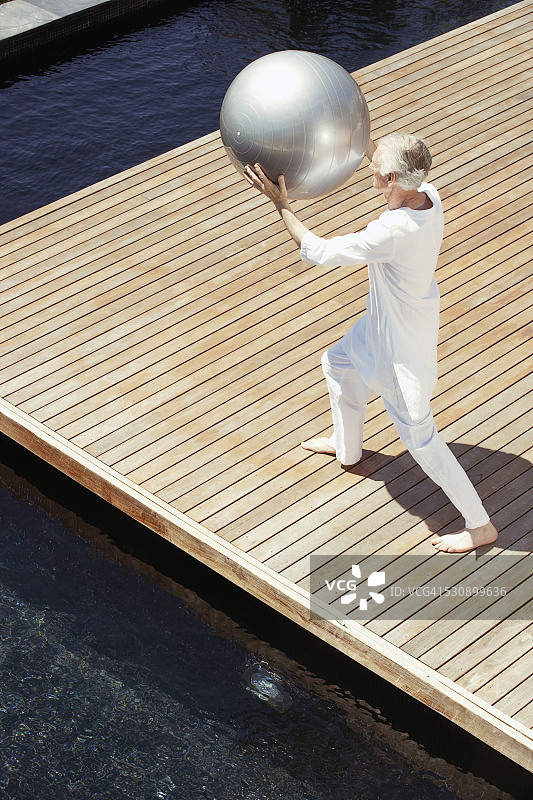 年长的男人在木制甲板上使用健身球图片素材