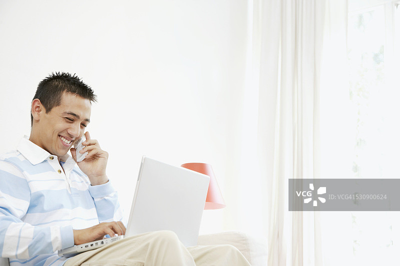年轻男人边用手机边使用笔记本电脑图片素材