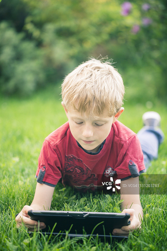 男孩躺在草地上使用平板电脑图片素材