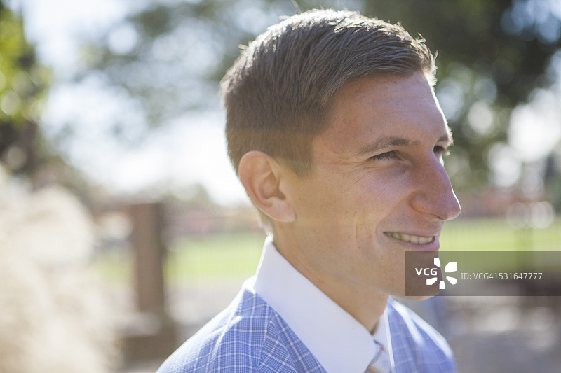 在阳光明媚的地方微笑的年轻男子的侧面照图片素材