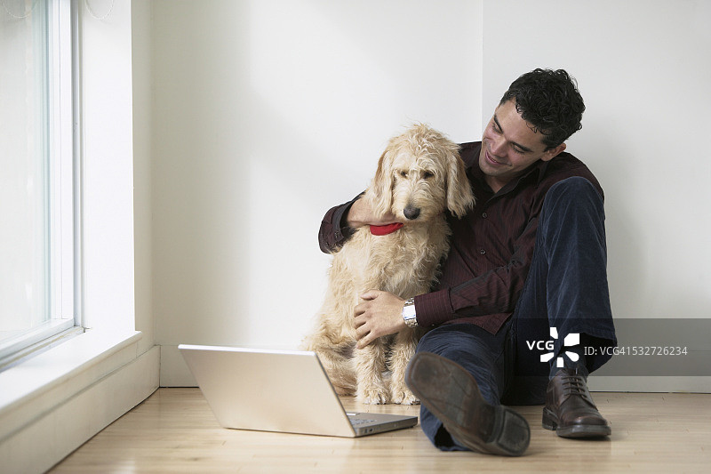 男人和小狗坐在地板上使用笔记本电脑图片素材