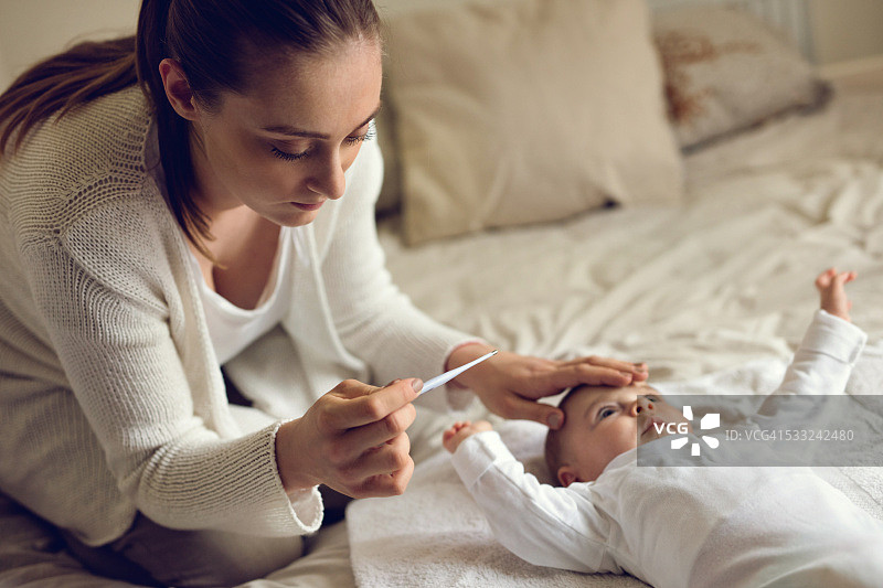 忧心忡忡的母亲在卧室测量宝宝的体温图片素材