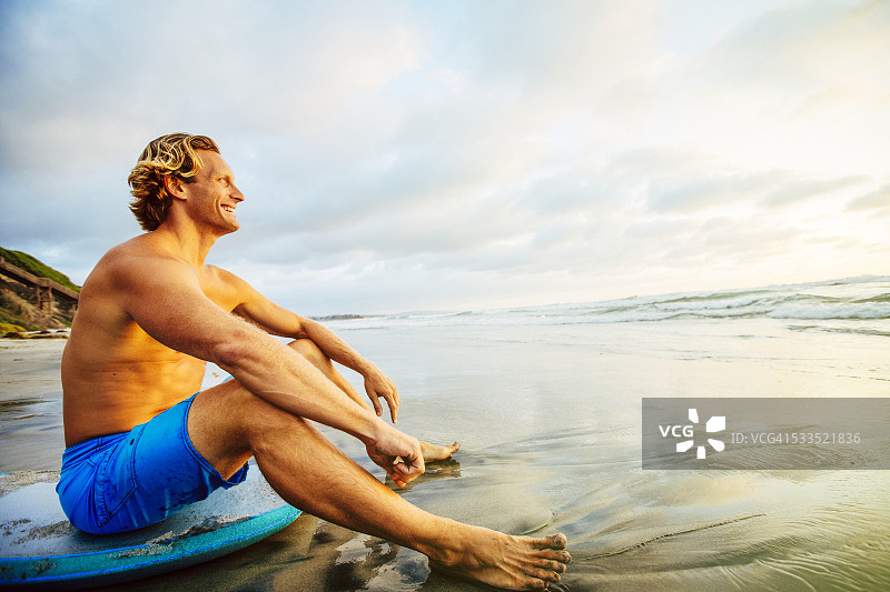 男人坐在冲浪板上，在海滩上看日落图片素材