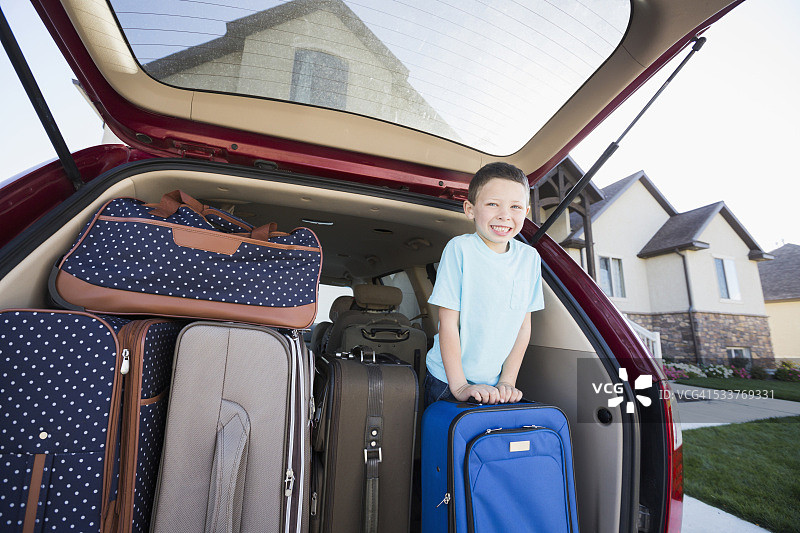 坐在车里，抱着行李箱微笑的白人男孩图片素材