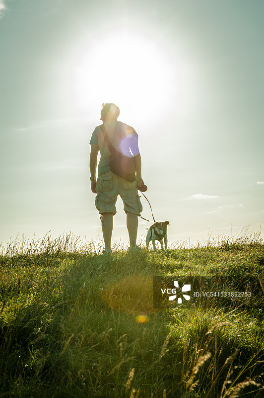 逆光下山顶上遛狗的男人图片素材