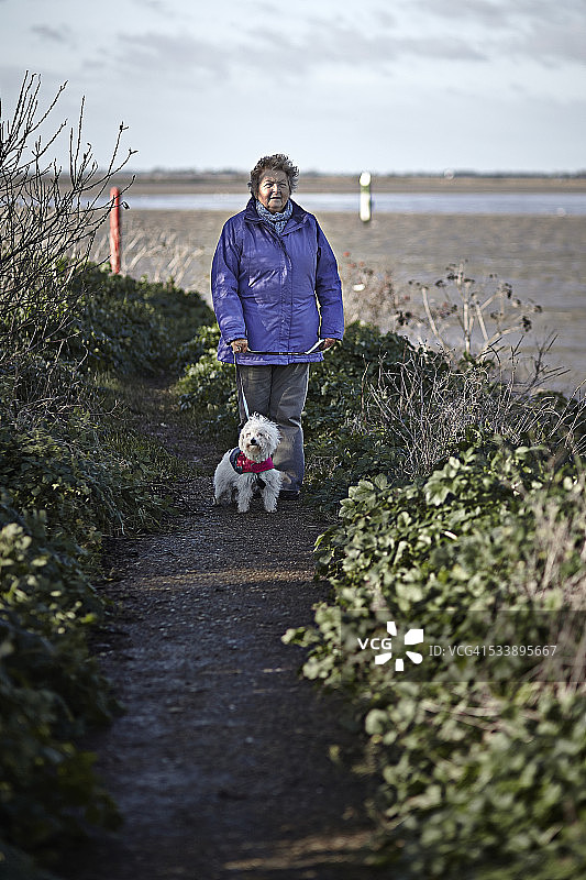 一位老年妇女站在河边的小路上图片素材