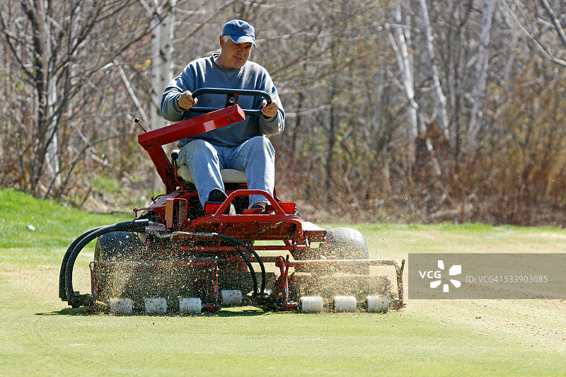 男人为高尔夫球场果岭进行垂直切割图片素材