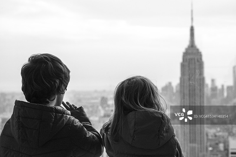 两个孩子透过窗户看纽约帝国大厦图片素材