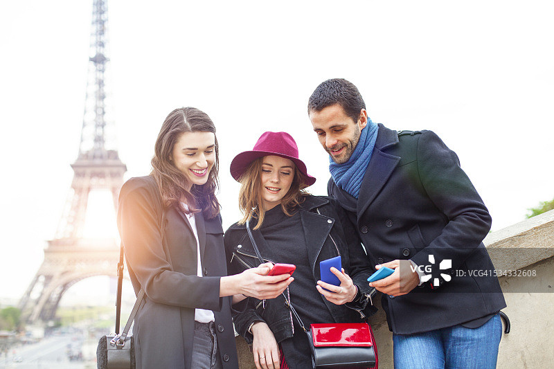 微笑的朋友们在埃菲尔铁塔附近使用智能手机图片素材