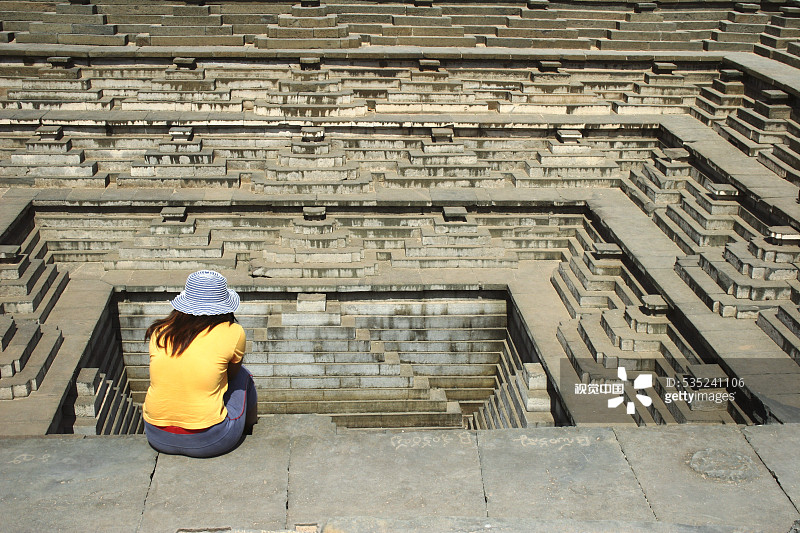 坐在印度卡纳塔克邦亨比维查耶那加尔遗址水池阶梯井旁的女人图片素材