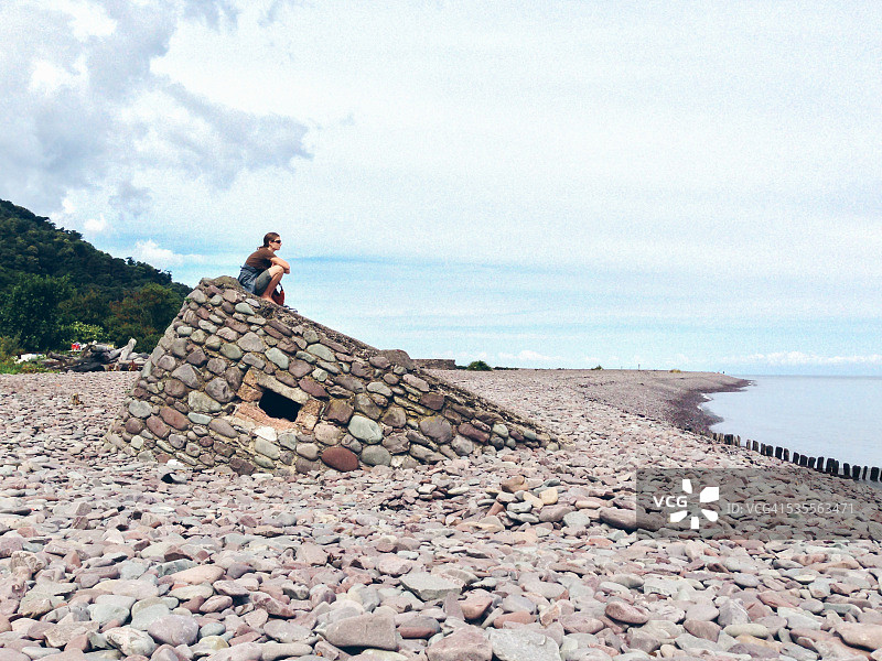 女人独自一人坐在海滩的石头掩体上图片素材