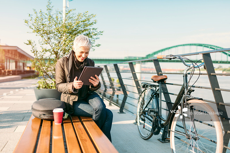 中年妇女坐着使用平板电脑喝咖啡图片素材