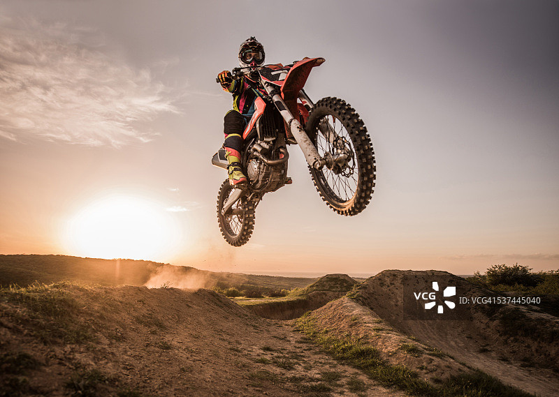 日落时分进行高跳跃的摩托车越野车手图片素材