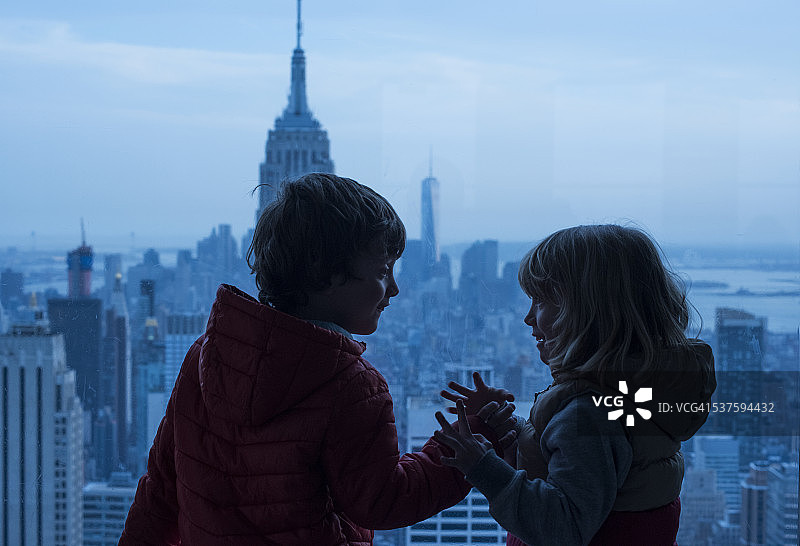 两个孩子隔窗相望，背景是纽约帝国大厦和自由塔图片素材