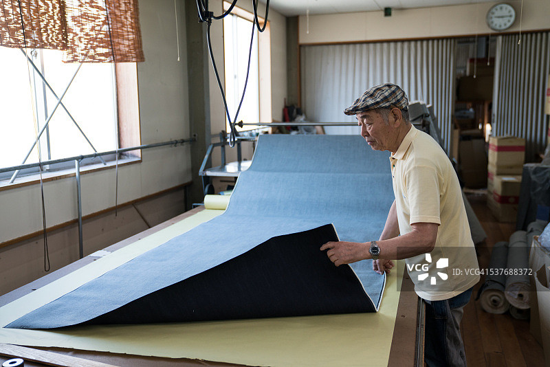 年长的裁缝展开牛仔布裁剪缝制牛仔裤图片素材