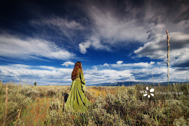 身穿中世纪礼服的女孩站在戏剧性的天空下的田野里图片素材
