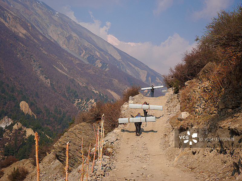 尼泊尔马南康萨尔：三名搬运工沿土路搬运锡板图片素材