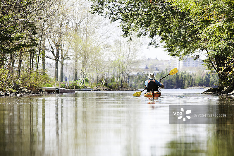 男人在城市湖泊的静水中划皮划艇图片素材