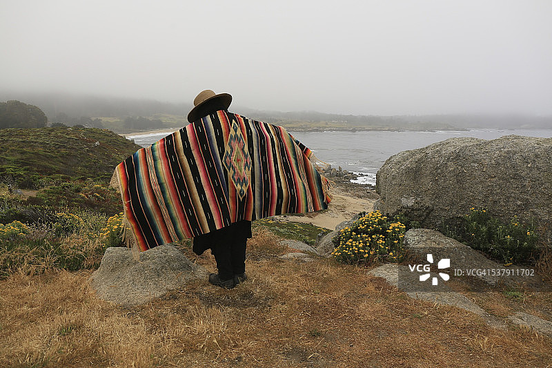 太平洋上方岩石上戴着古董披肩和草帽的人图片素材
