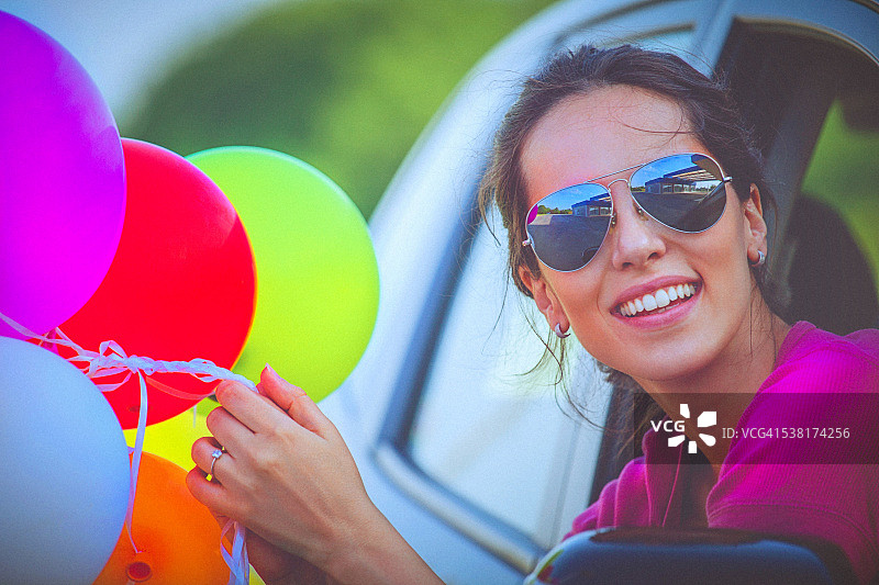 快乐的女人拿着彩色气球，从车窗向外看图片素材