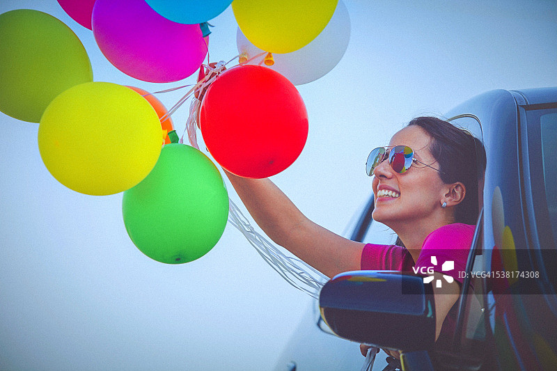 快乐的女人拿着彩色气球，从车窗向外看图片素材